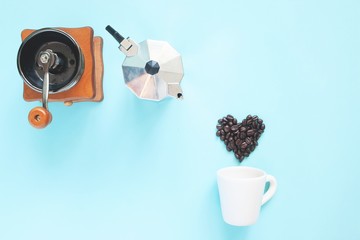 Creative flat lay of heart shape coffee beans and coffee grinder and pot on blue colour background