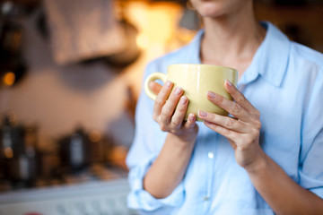Graceful female hands hold cup of tea. Young woman is drinking coffee in cozy home kitchen. Close up.