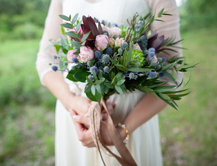 Beautiful rustic style in wedding decor. Closeup view of hands of bride holding beautiful bunch of...