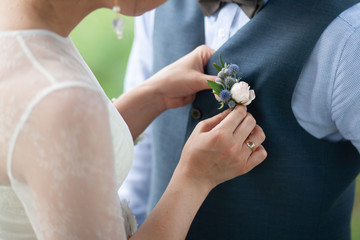 Beautiful rustic style in wedding decor. Bride attaching small boutonniere to vest. Horizontal color photography. - obrazy, fototapety, plakaty