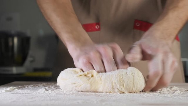 Chef baker is kneading dough with flour by hands on the table. Hands close-up.