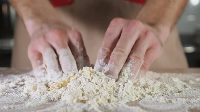 Chef baker is kneading dough with flour by hands on the table, close-up.