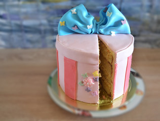 Delicious tangerine cake with original decor made of mastic in the form of a pink gift box with a blue bow. Delicious birthday dessert.