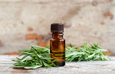 Small bottle of essential rosemary oil on the old wooden background. Aromatherapy, spa and herbal...
