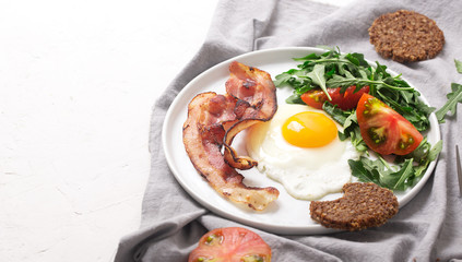 Hearty high protein english style breakfast with egg, fried bacon and arugula on the plate. Top view, horizontal orientation