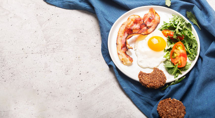 Hearty high protein english style breakfast with egg, fried bacon and arugula on the plate. Top...