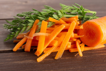 One half lot of pieces of fresh orange carrot cut into thin noodles with greens on brown wood