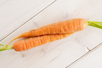 Group of two whole fresh orange carrot with greens flatlay on white wood