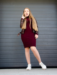 Portrait of a beautiful girl in a dark red dress knee-deep and in a dark leather jacket in the street in the afternoon