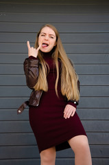 Portrait of a beautiful girl in a dark red dress knee-deep and in a dark leather jacket in the street in the afternoon