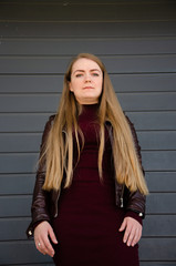 Portrait of a beautiful girl in a dark red dress knee-deep and in a dark leather jacket in the street in the afternoon