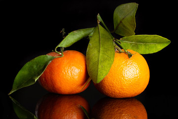 Group of two whole bright fresh orange mandarine with green leaves isolated on black glass