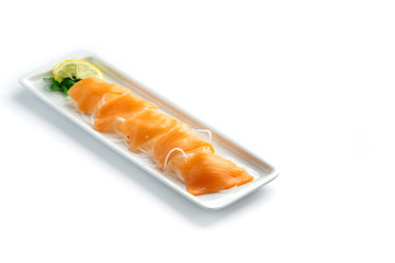 pieces of red fish with lemon and herbs on a rectangular plate on an isolated white background