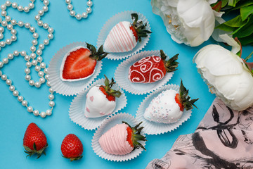 Fresh strawberries covered with white and pink chocolate, white flowers and pearl beads lie on a turquoise background