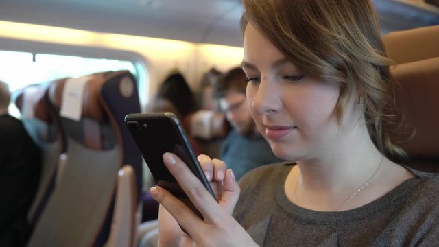 Young girl using smartphone, serfing internet. Passenger in train.