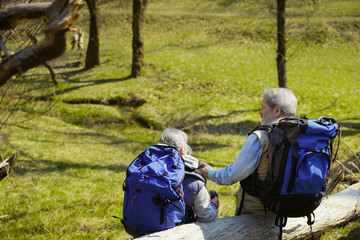 Fototapeta na wymiar Planning future. Aged family couple of man and woman in tourist outfit walking at green lawn near by trees and creek in sunny day. Concept of tourism, healthy lifestyle, relaxation and togetherness.