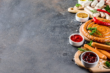 Set of various sausages ready for grilling, with different sauces, black concrete background copy space