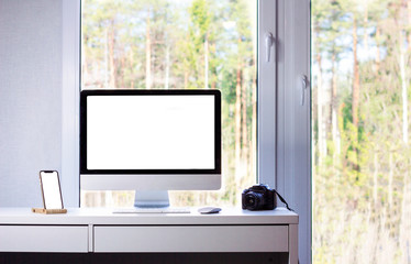 Mock up of a phone and a computer. Desktop of a photographer: computer, camera, phone, mouse and keyboard, window with summer forest outside, minimalism, the room of freelancer, minimalist flat