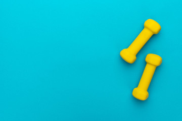 flat lay photo of yellow fitness dumbells over blue backgound with copy space