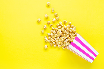 Striped paper cup with popcorn on yellow background. Top view. Copy space