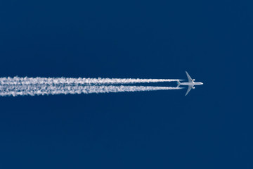 Airplane flies leaving contrail trace on a clear high blue sky.