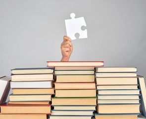 female hand holding a big white puzzle and a stack of books