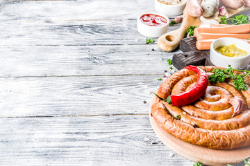 Set of various sausages ready for grilling, with different sauces, white wooden background copy space