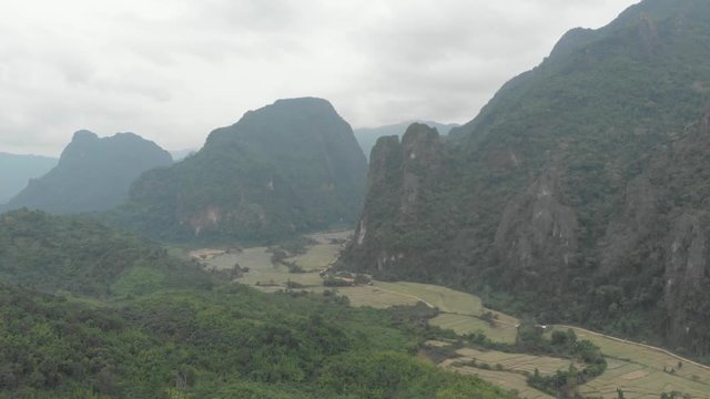 Aerial: flying over scenic cliffs rock pinnacles tropical jungle rice paddies valley stunning landscape around Vang Vieng popular destination in Laos Asia. Native cinelike D-log color profile