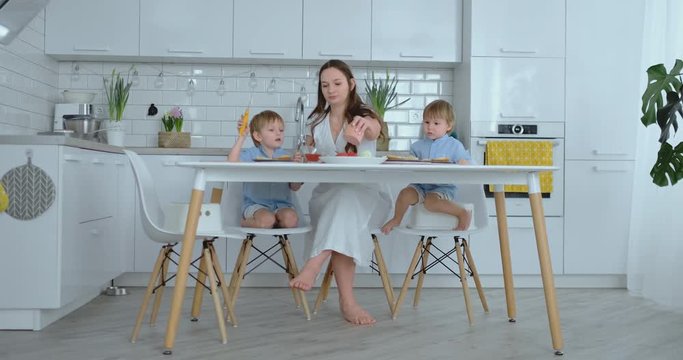 Beautiful young mother with two children sons on white light kuna cook with burgers