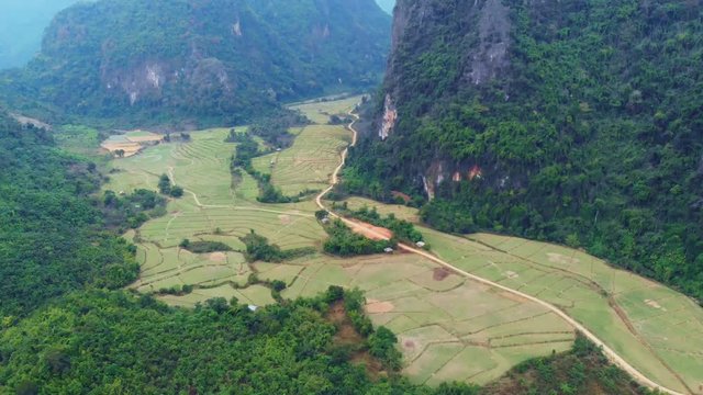 Aerial: flying over scenic cliffs rock pinnacles tropical jungle rice paddies valley stunning landscape around Vang Vieng popular destination in Laos Asia