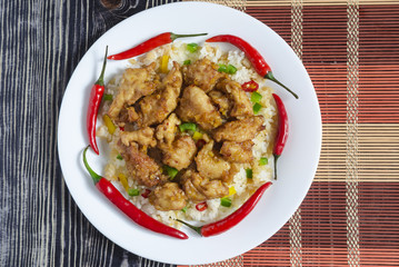 chicken in sweet and sour sauce and rice with vegetables and pepper on a white plate background of two colors