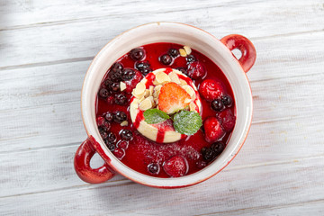 Homemade strawberries cheesecake with berries  syrup and mint on red bowl on white wooden background, top view