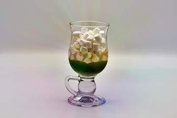 Coffee and many small marshmallows in a transparent glass cup on a gray background. With rays coming from the cup
