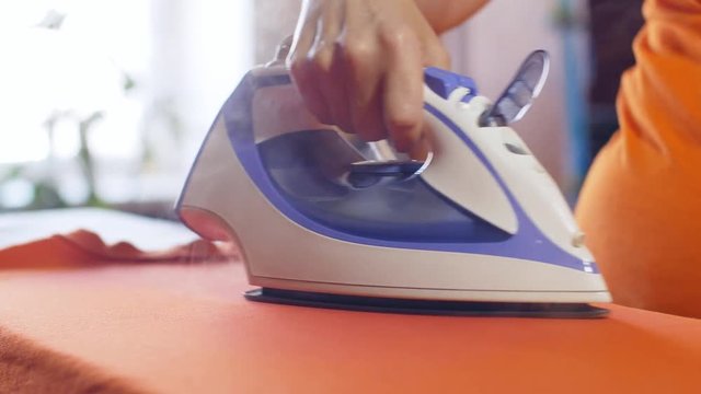 Woman ironing an orange shirt with a steam iron