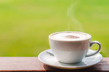 Hot coffee placed on the wooden table in early morning with copyspace, white cup and silver spoon. The green background with defocus effect.