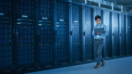 In the Modern Data Center: IT Engineer Working with Server Racks, Uses Laptop for Maintenance and...