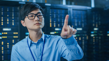 In the Modern Data Center: Portrait of IT Engineer Working With Touch Screen Device, Doing Touching Gesture. In the Background Working Server Racks with Blinking LED Lights.