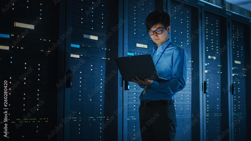 Leinwandbilder in dark data center: male it specialist walks along the row of operational server racks, uses laptop