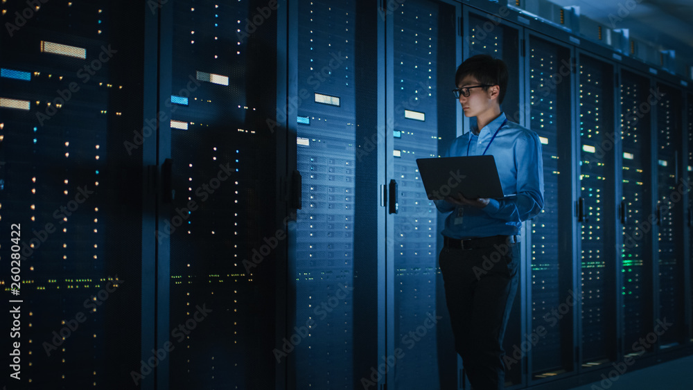 Aufkleber in dark data center: male it specialist walks along the row of operational server racks, uses laptop