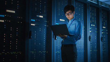 In Dark Data Center: Male IT Specialist Walks along the Row of Operational Server Racks, Uses...