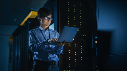 In Dark Data Center: Male IT Specialist Stands Beside the Row of Operational Server Racks, Uses Laptop for Maintenance. Concept for Cloud Computing, Artificial Intelligence, Cybersecurity. Neon Lights