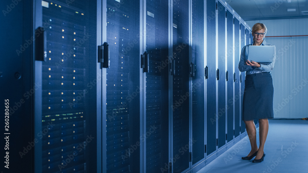 Leinwandbilder In Data Center: Female IT Technician Running Maintenance Programme on a Laptop, Controls Operational Server Rack Optimal Functioning. Modern High-Tech Telecommunications Operational Super Computer.