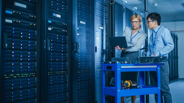 In the Modern Data Center: Engineer and IT Specialist Work with Server Racks, on a Pushcart Equipment for Installing New Hardware. Specialists Doing Maintenance and Diagnostics of the Database.