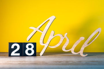 April 28th. Day 28 of month, calendar on wooden table and green background. Spring time, empty space for text