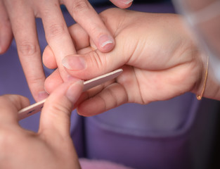 Obraz na płótnie Canvas Woman receiving fingernail manicure service by professional manicurist at nail salon. Beautician file nail manicure at nail and spa salon. Hand care and fingernail treatment at nail salon.