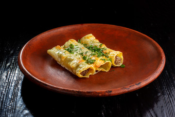 Hot folded pancakes with beef and greens on black wooden background. Laid out on a clay plate.
