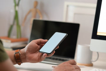 Blank screen mock up mobile phone in man hand at home office.