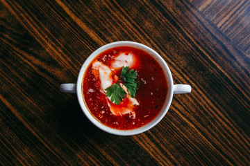Christmas beetroot soup, borscht with small dumplings with mushroom filling in a ceramic bowl on a wooden table.