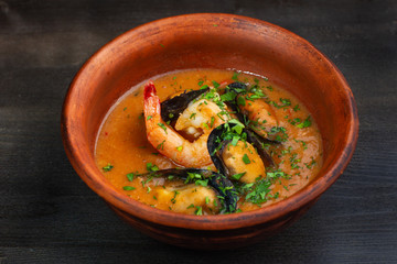 Spicy french soup with seafood in a clay plate.