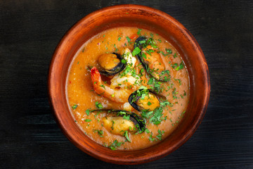 Spicy french soup with seafood in a clay plate.